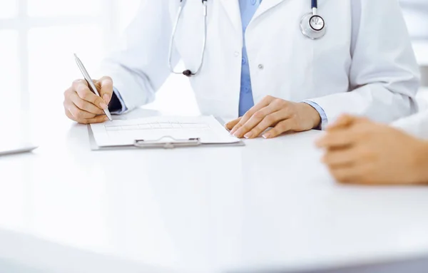 Onbekende vrouw-dokter en vrouwelijke patiënt zitten en praten bij medisch onderzoek in de kliniek, close-up. Therapeut met blauwe blouse vult de geschiedenis van medicatie. Geneesmiddelenconcept — Stockfoto