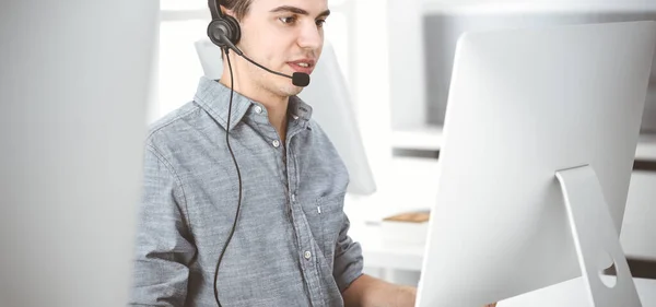 Casual vestido jovem usando fone de ouvido e computador enquanto conversa com clientes on-line. Call center, conceito de negócio — Fotografia de Stock