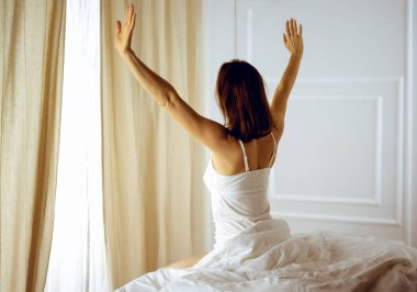 Bir kadın uyandıktan sonra yatakta geriniyor, geriye bakıyor, bir güne mutlu ve rahat giriyor iyi bir gece uykusundan sonra. Esmer için günaydın ve yeni bir gün. Hafta sonu kavramı, tatiller