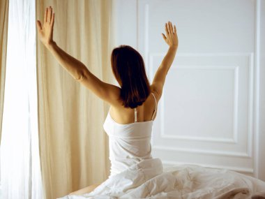 Bir kadın uyandıktan sonra yatakta geriniyor, geriye bakıyor, bir güne mutlu ve rahat giriyor iyi bir gece uykusundan sonra. Esmer için günaydın ve yeni bir gün. Hafta sonu kavramı, tatiller