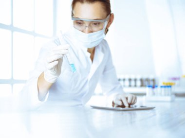 Kadın laboratuvar asistanı mavi sıvıyla test tüpünü analiz ediyor. Tıp, sağlık ve araştırma konsepti