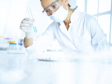 Kadın laboratuvar asistanı mavi sıvıyla test tüpünü analiz ediyor. Tıp, sağlık ve araştırma konsepti