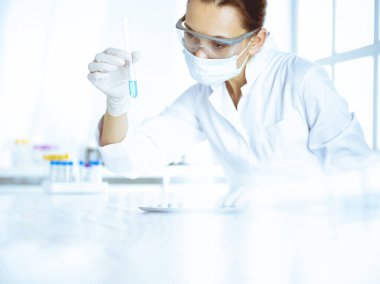 Kadın laboratuvar asistanı mavi sıvıyla test tüpünü analiz ediyor. Tıp, sağlık ve araştırma konsepti