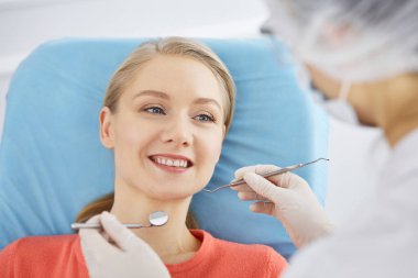 Gülümseyen beyaz kadın dişçi kliniğinde dişçi tarafından muayene ediliyor. Sağlıklı dişler ve ilaçlar, stomatoloji konsepti
