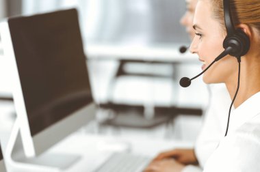 Sarışın kadın müşteri hizmetleri temsilcisi ve meslektaşı internetteki müşterilerine kulaklık kullanarak danışıyorlar. Çağrı merkezi ve iş adamları kavramı