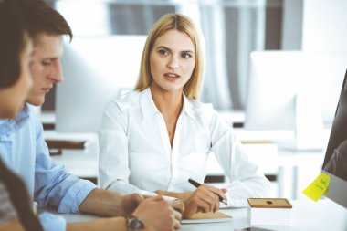 Bir grup iş adamı toplantıda soruları tartışıyor. Ofis görüşmelerinde iş arkadaşına gülümseyen sarışın iş kadınının vesikalığı. Şirket işgalinde takım çalışması ve işbirliği