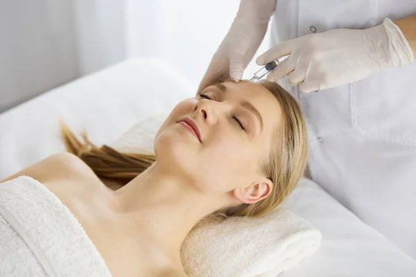 Beautician doctor doing beauty procedure with syringe to caucasian female face. Cosmetic medicine and surgery, beauty injections concept