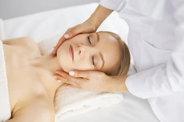 Güzel beyaz kadın spa salonunda gözleri kapalı yüz masajından zevk alıyor. Tıp ve Güzellik konseptinde rahatlatıcı tedavi — Stok fotoğraf