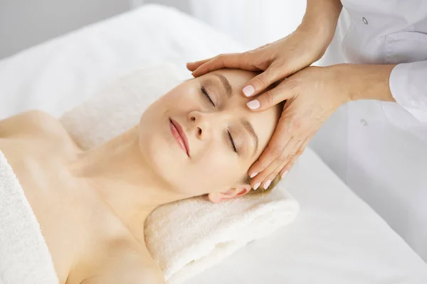 Hermosa mujer caucásica disfrutando de masaje facial con los ojos cerrados en el salón de spa. Tratamiento relajante en medicina y concepto de belleza — Foto de Stock