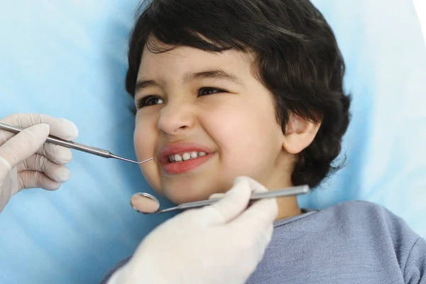 Lindo chico árabe sentado en la silla dental con la boca abierta durante el control oral con el médico. Visita al consultorio del dentista. Concepto de estomatología — Foto de Stock