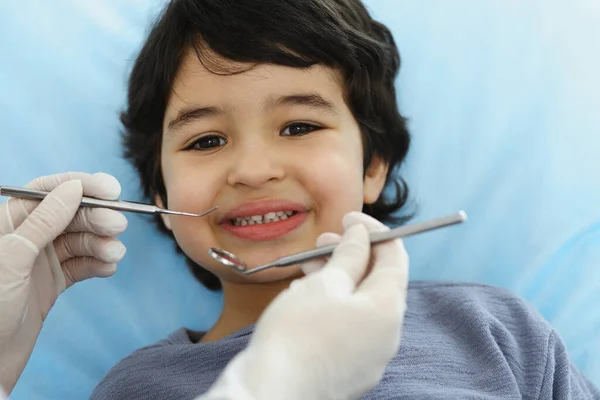 Cute chłopiec arabski siedzi na krześle dentystycznym z otwartymi ustami podczas badania doustnego z lekarzem. Odwiedzam gabinet dentystyczny. Koncepcja stomatologii — Zdjęcie stockowe