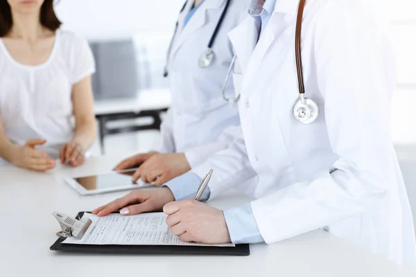 Okända kvinnliga läkare på jobbet konsulterar patienten. Kvinnliga läkare fylla upp medicinska dokument eller recept, närbild — Stockfoto
