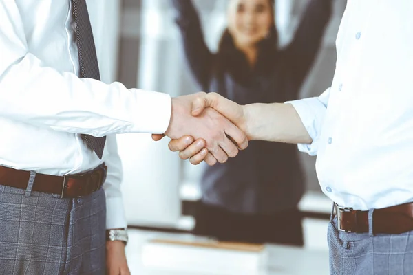 Two businessmen are shaking hands in office, close-up. Happy and excited business woman stands with raising hands at the background. Business people concept — Stock Photo, Image