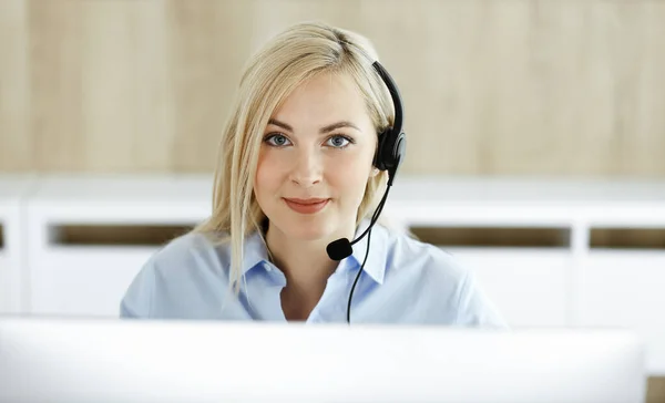 コールセンターのオフィスでヘッドセットで座って通信しているブロンドのビジネス女性。テレセールス事業又は住宅事業の概念 — ストック写真