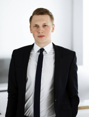 Ofisteki kameraya bakıp duran neşeli iş adamı. Genç ve başarılı girişimcinin vesikalığı