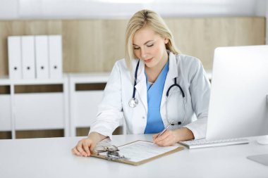Hastanedeki ya da klinikteki masa başında oturan kadın doktor. Sarışın, neşeli doktor ilaç geçmişi formunu dolduruyor.