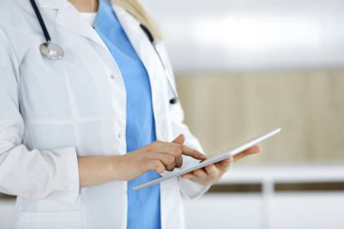 Bilinmeyen kadın doktor klinikte duruyor ve tablet bilgisayar kullanıyor, yakın plan. Tıp ve sağlık alanlarındaki veriler