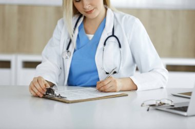 İş yerindeki bilinmeyen kadın-doktor klinikte ilaç geçmişi formunu dolduruyor, panonun yakın çekimini yapıyor.