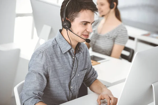 在网上与顾客交谈时，用耳机和电脑随意穿衣的年轻人。一组操作员在工作。呼叫中心 — 图库照片