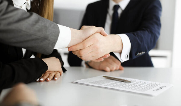 Неизвестный бизнесмен пожимает руку коллеге или партнеру над стеклянным столом в современном офисе крупным планом. Группа деловых людей на встрече