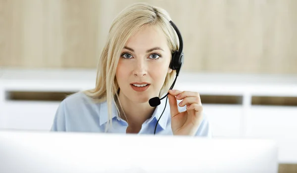 Blonde business woman sitting and communicated by headset in call center office. Concept of telesales business or home office occupation Royalty Free Stock Photos