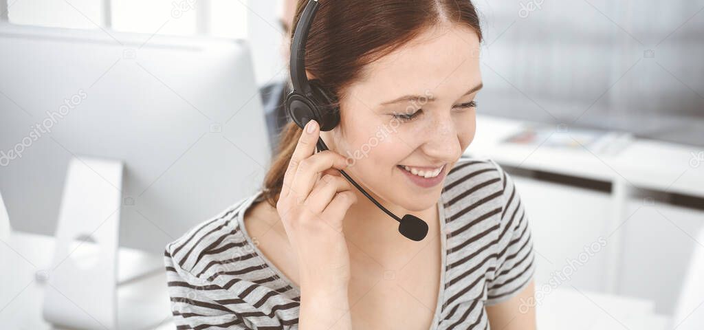 Casual dressed young woman using headset and computer while talking with customers online. Group of operators at work. Call center, business concept