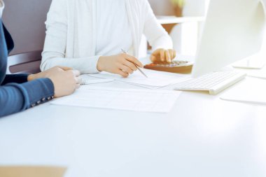 Muhasebeci mali durumu kontrol ediyor ya da vergi formları için hesap makinesi geliri ile sayıyor, eller yakın çekim. İş kadını ofisteki masada iş arkadaşıyla oturuyor ve çalışıyor. Denetim kavramı