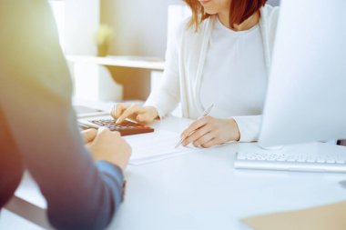 Muhasebeci mali durumu kontrol ediyor ya da vergi formları için hesap makinesi geliri ile sayıyor, eller yakın çekim. İş kadını ofisteki masada iş arkadaşıyla oturuyor ve çalışıyor. Denetim kavramı