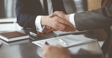 Bilinmeyen işadamı, modern ofiste iş arkadaşı ya da ortağıyla el sıkışıyor. Toplantıda iş adamları grubu