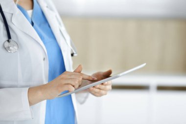 Bilinmeyen kadın doktor klinikte duruyor ve tablet bilgisayar kullanıyor, yakın plan. Tıp ve sağlık alanlarındaki veriler
