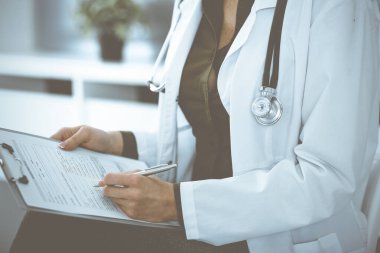 Bilinmeyen kadın doktor panoya bir şeyler yazıyor. Sandalyede otururken, yakın plan. İş yerinde yeşil bluz giyen terapist ilaç geçmişini dolduruyor. Tıp konsepti