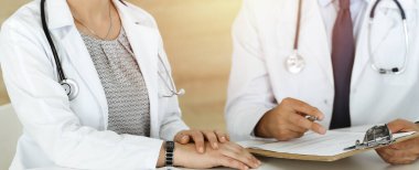 Güneşli hastane ofisindeki masada otururken tedavi sorunlarını tartışan iki bilinmeyen doktor.