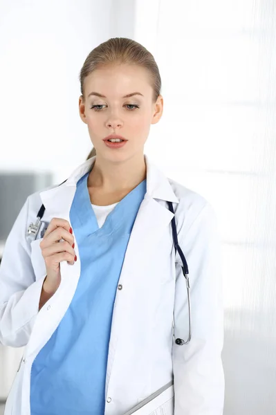 Nő - orvos áll a klinikán. Orvos a munkahelyén, műtermi portré. Orvosi és egészségügyi ellátás fogalma — Stock Fotó