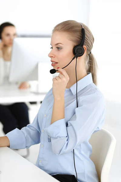 Mujer rubia operador de llamadas está utilizando la computadora y auriculares para consultar a los clientes en línea. Grupo de personas diversas que trabajan como ocupación de servicio al cliente. Concepto empresarial —  Fotos de Stock