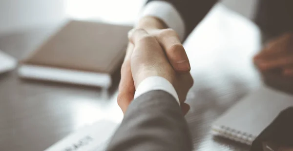 Hombre de negocios desconocido estrechando la mano con su colega o compañero por encima del escritorio de cristal en la oficina moderna, de cerca. Grupo de empresarios en la reunión — Foto de Stock