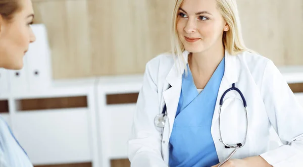 Mujer-médico y paciente sentados y hablando en el hospital o clínica. La terapeuta rubia sonríe alegremente. Concepto de medicina — Foto de Stock