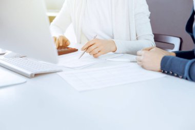 Muhasebeci mali durumu kontrol ediyor ya da vergi formları için hesap makinesi geliri ile sayıyor, eller yakın çekim. İş kadını ofisteki masada iş arkadaşıyla oturuyor ve çalışıyor. Denetim kavramı