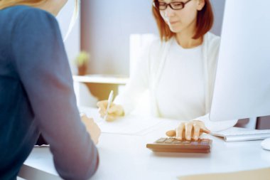 Muhasebeci mali durumu kontrol ediyor ya da vergi formları için hesap makinesi geliri ile sayıyor, eller yakın çekim. İş kadını ofisteki masada iş arkadaşıyla oturuyor ve çalışıyor. Denetim kavramı