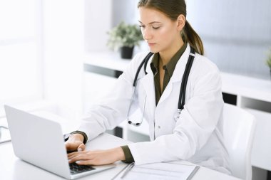 Hastane ofisindeki masada otururken dizüstü bilgisayarda yazan bir kadın doktor. Hekim iş başında. Tıp ve sağlık alanlarındaki veriler