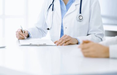 Bilinmeyen kadın-doktor ve kadın hasta klinikteki tıbbi muayenede oturuyor ve konuşuyor, yakın plan. Mavi bluz giyen terapist ilaç geçmişini dolduruyor. Tıp konsepti