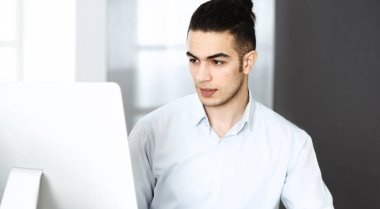 İşadamı modern ofiste bilgisayarla çalışıyor. Arap erkek girişimcinin iş yerindeki portresi. İş konsepti