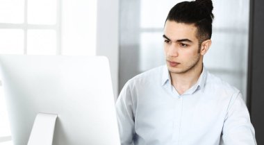 İşadamı modern ofiste bilgisayarla çalışıyor. Arap erkek girişimcinin iş yerindeki portresi. İş konsepti