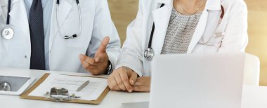 Güneşli hastane ofisindeki masada otururken tedavi sorunlarını tartışan iki bilinmeyen doktor.