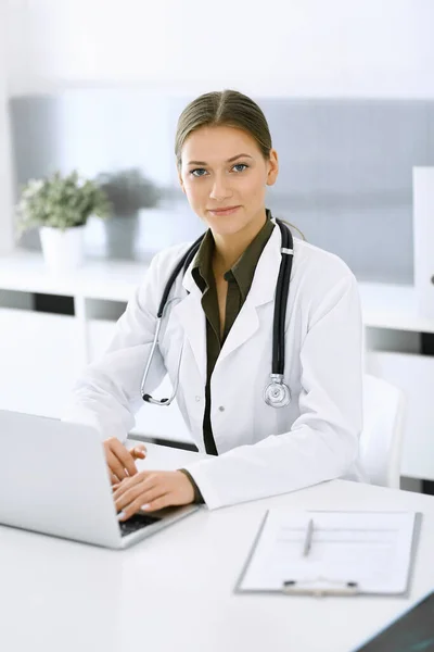 Mujer-médico escribiendo en el ordenador portátil mientras está sentado en el escritorio en la oficina del hospital. Médico trabajando. Datos en medicina y asistencia sanitaria — Foto de Stock