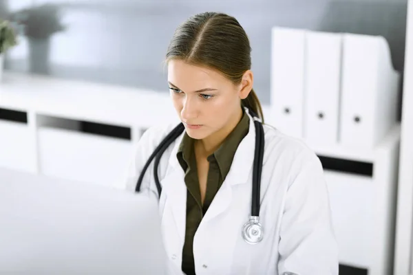 Mujer-médico escribiendo en la computadora PC mientras está sentado en el escritorio en la oficina del hospital. Médico trabajando. Datos en medicina y asistencia sanitaria — Foto de Stock