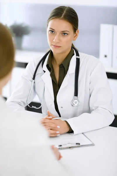 Woman-doctor and patient sitting and talking at hospital office. Green color blouse suits to therapist. Medicine and healthcare concept — Stock Photo, Image