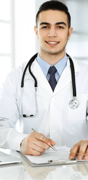 Arab doctor man is using laptop computer while filling up medication history records form at the glass desk in r clinic. Medicine concept — Stock Photo, Image