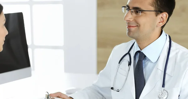 Médico e paciente discutindo os resultados do exame médico enquanto estava sentado na mesa na clínica. Médico masculino usando prancheta para preencher o registro de histórico de medicação de mulher jovem. Dados em medicina — Fotografia de Stock