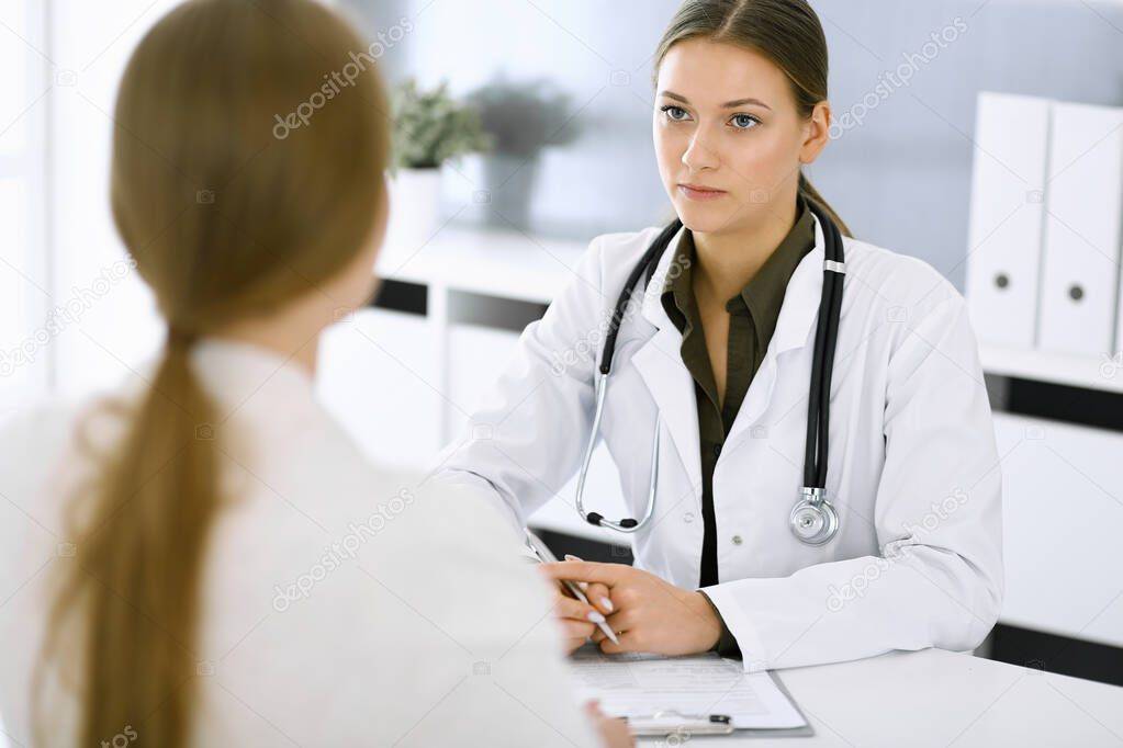Woman-doctor and patient sitting and talking at hospital office. Green color blouse suits to therapist. Medicine and healthcare concept
