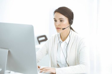 Merkezi ara. Müşteri hizmetlerinde kulaklık takan sıradan giyinmiş bir kadın. Bir grup operatör iş başında. İş konsepti